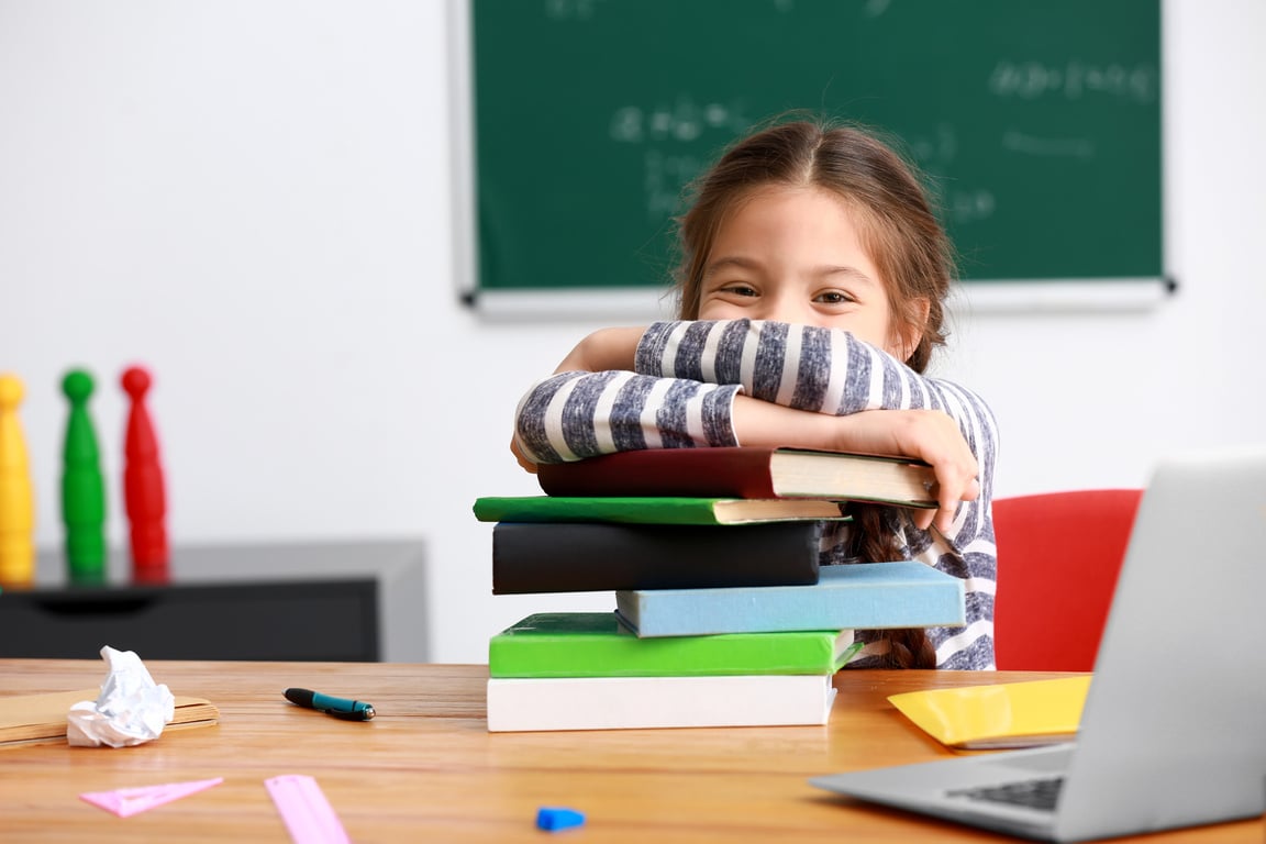 Cute Girl with Stack of Books Sitting in Classroom